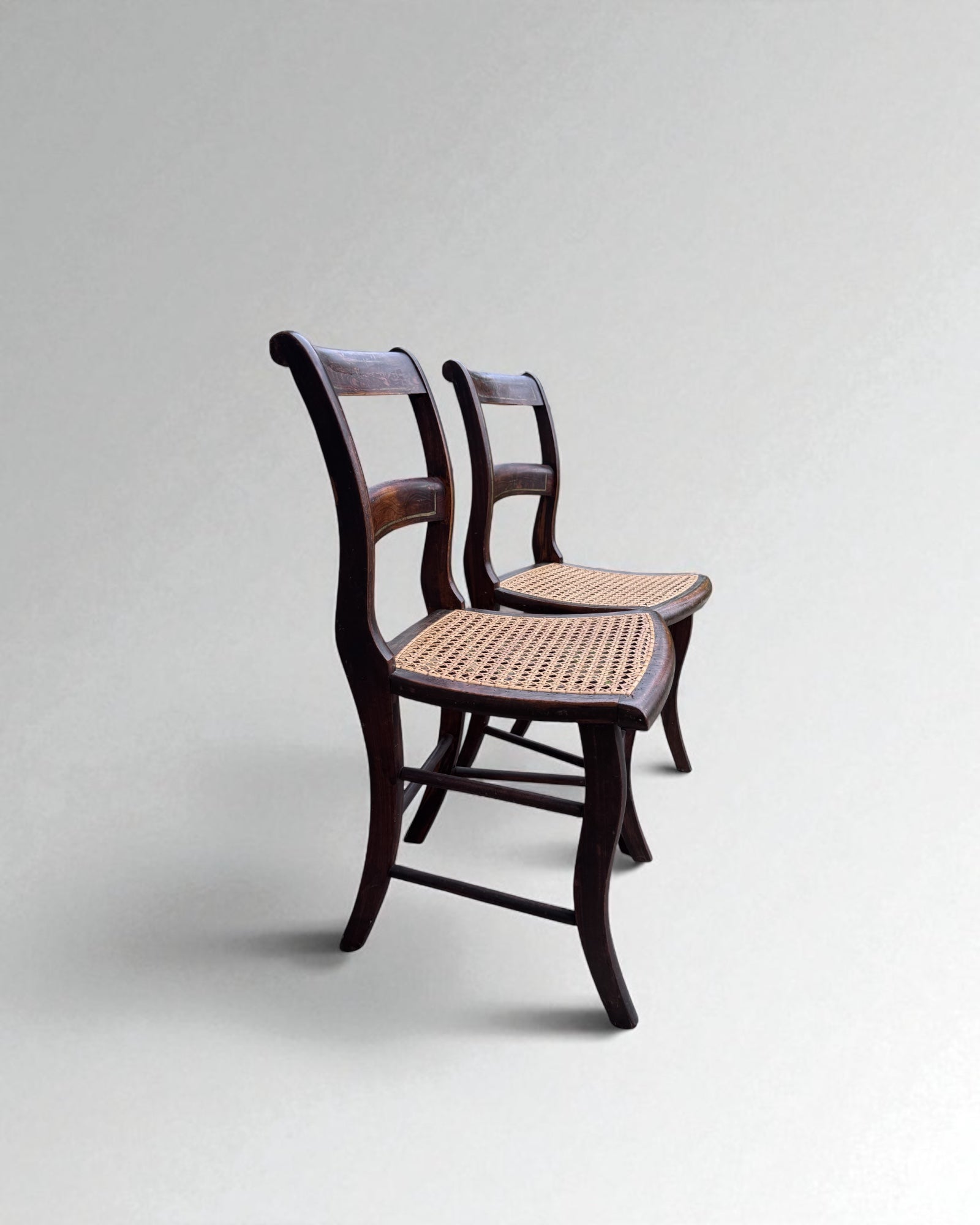Pair of caned dining chairs with woven seats on a light gray background