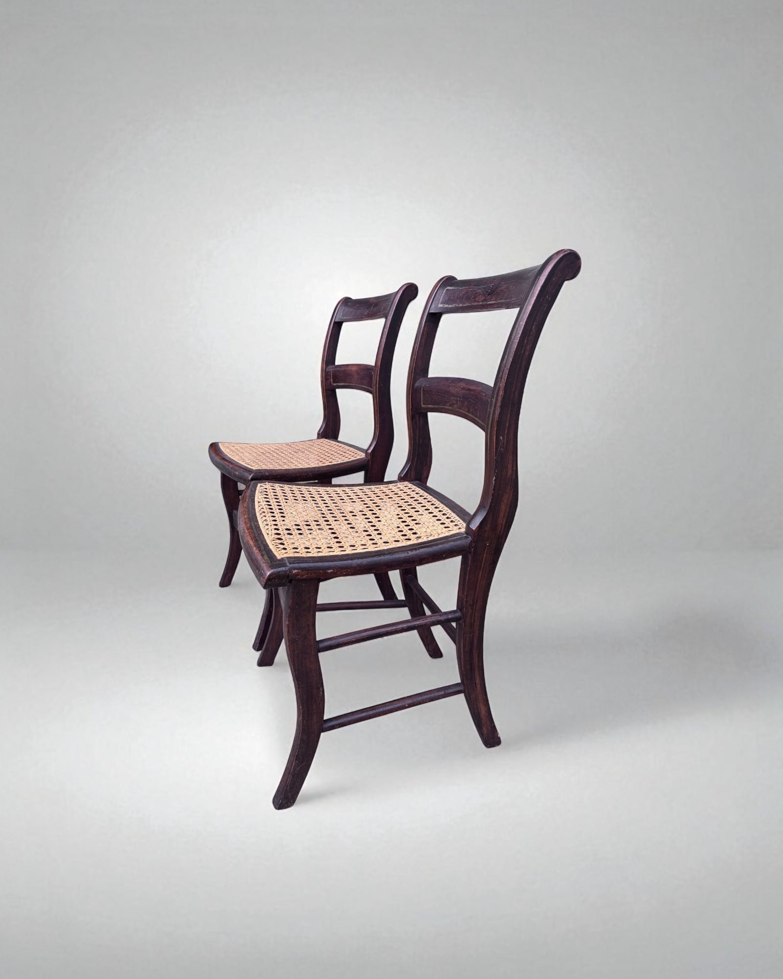 Two wooden caned dining chairs with woven seats on a light gray background