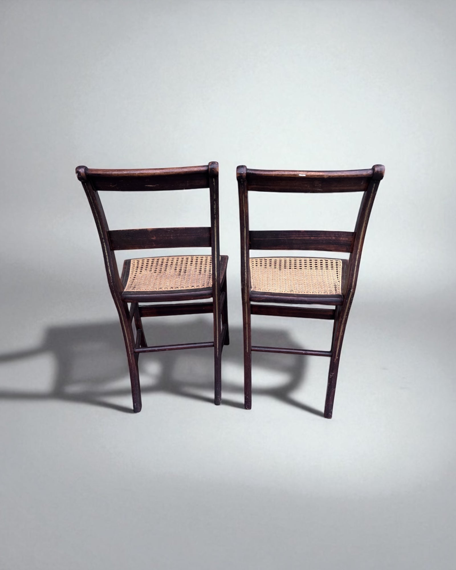 Two caned dining chairs with woven seats on a gray background